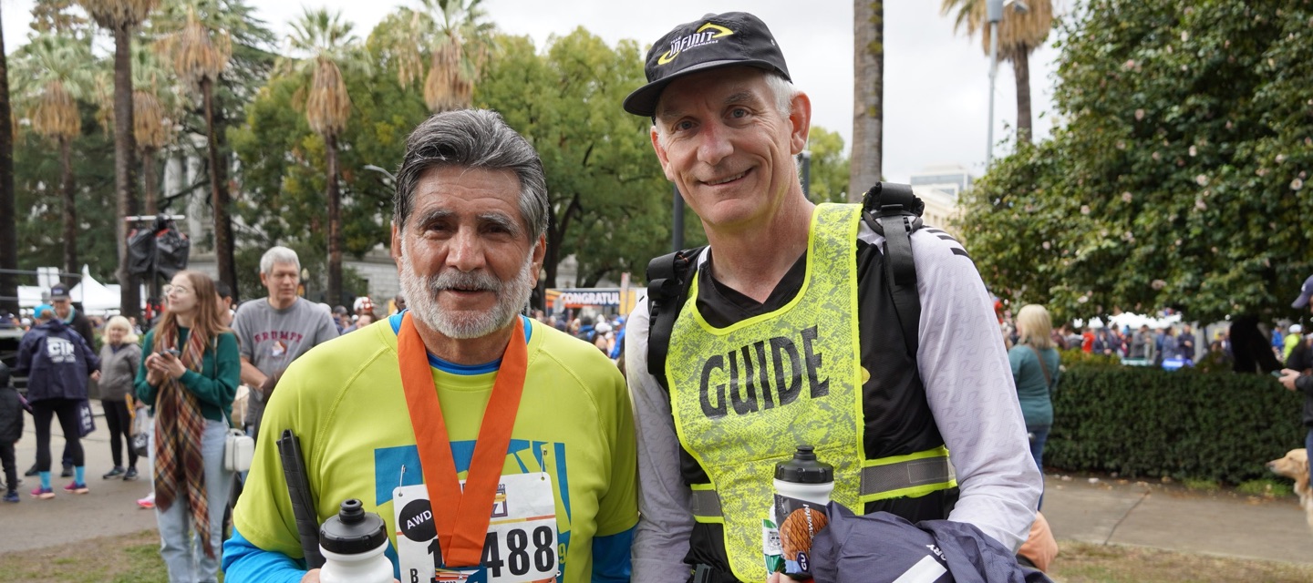 Visually Impaired runner and guide posing with their medals after a race.