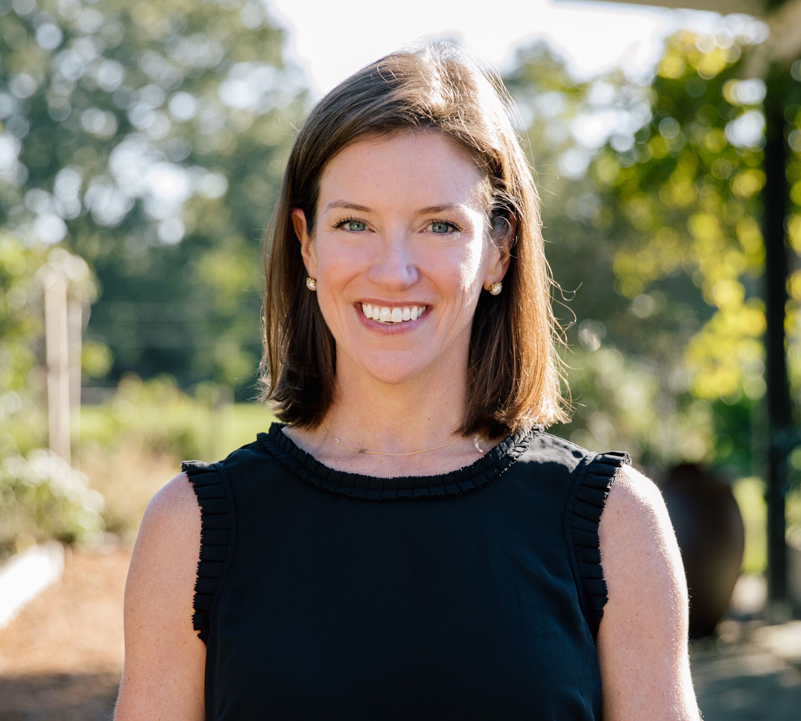 A smiling woman in a black dress in an outdoor setting with trees in the background